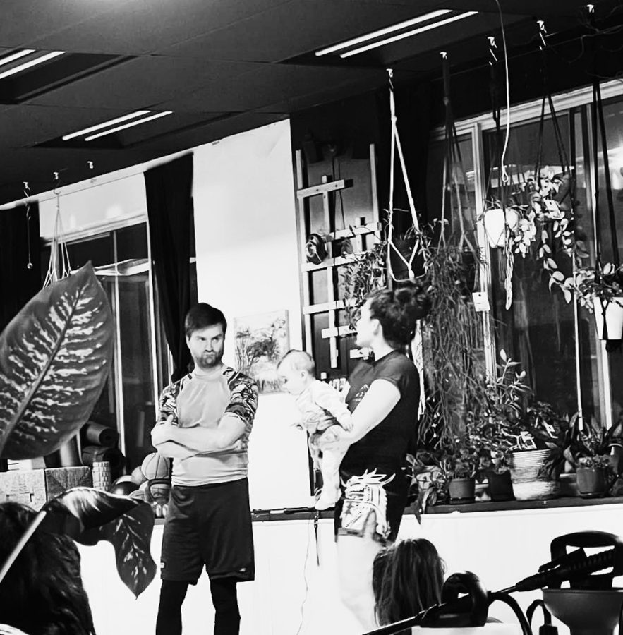Un instructeur discute avec une élève qui tient son bébé, entourée de plantes, avant un cours d'introduction au BJJ