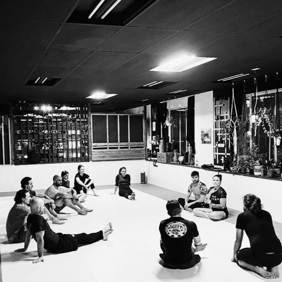 Élèves assis en cercle sur le tatami pendant l'échauffement d'un cours d'introduction au BJJ