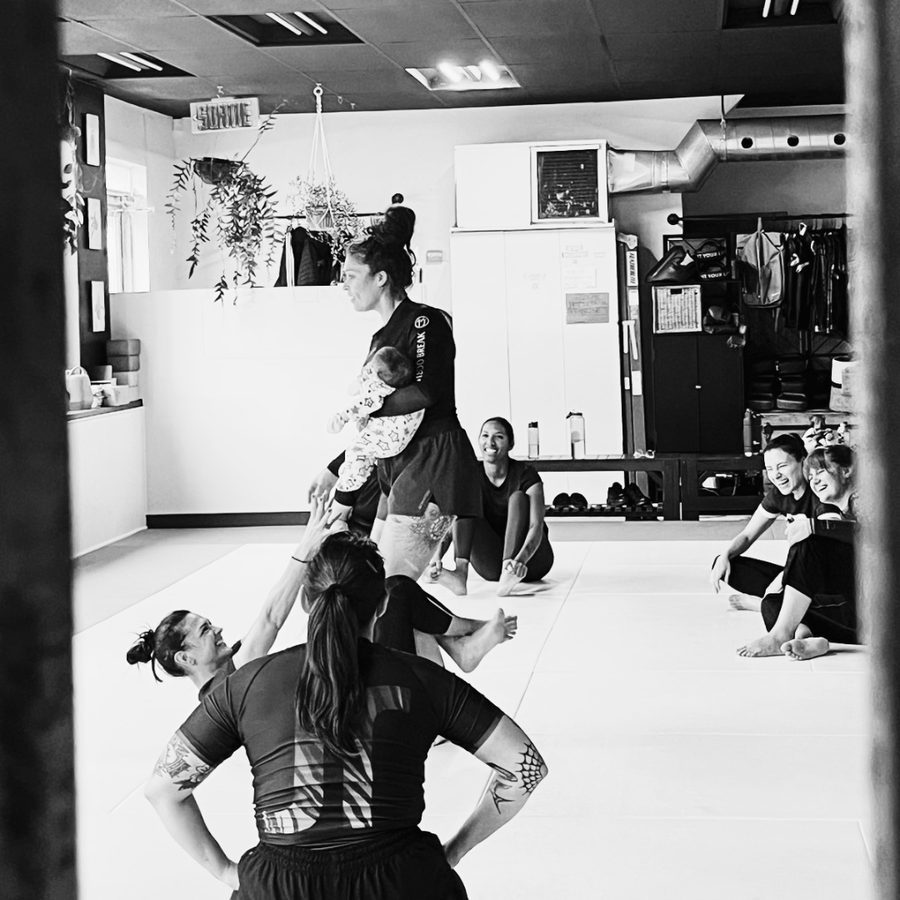 Une élève soulève son bébé au-dessus du tatami pendant un cours d'introduction, sous les rires du groupe